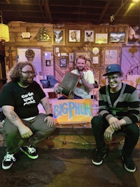 three men posing in front of a big pig sign